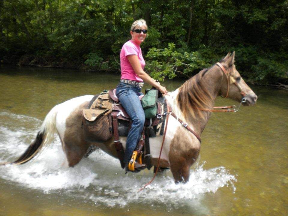 Deanna horseback riding through a creek